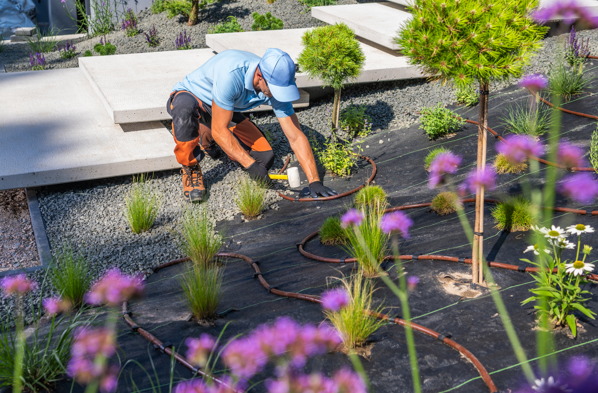 Landscaper using durable outdoor work gloves while trimming bushes, versatile gardening gloves and yard work gloves with reinforced palms and 500-lb finger guard protection.